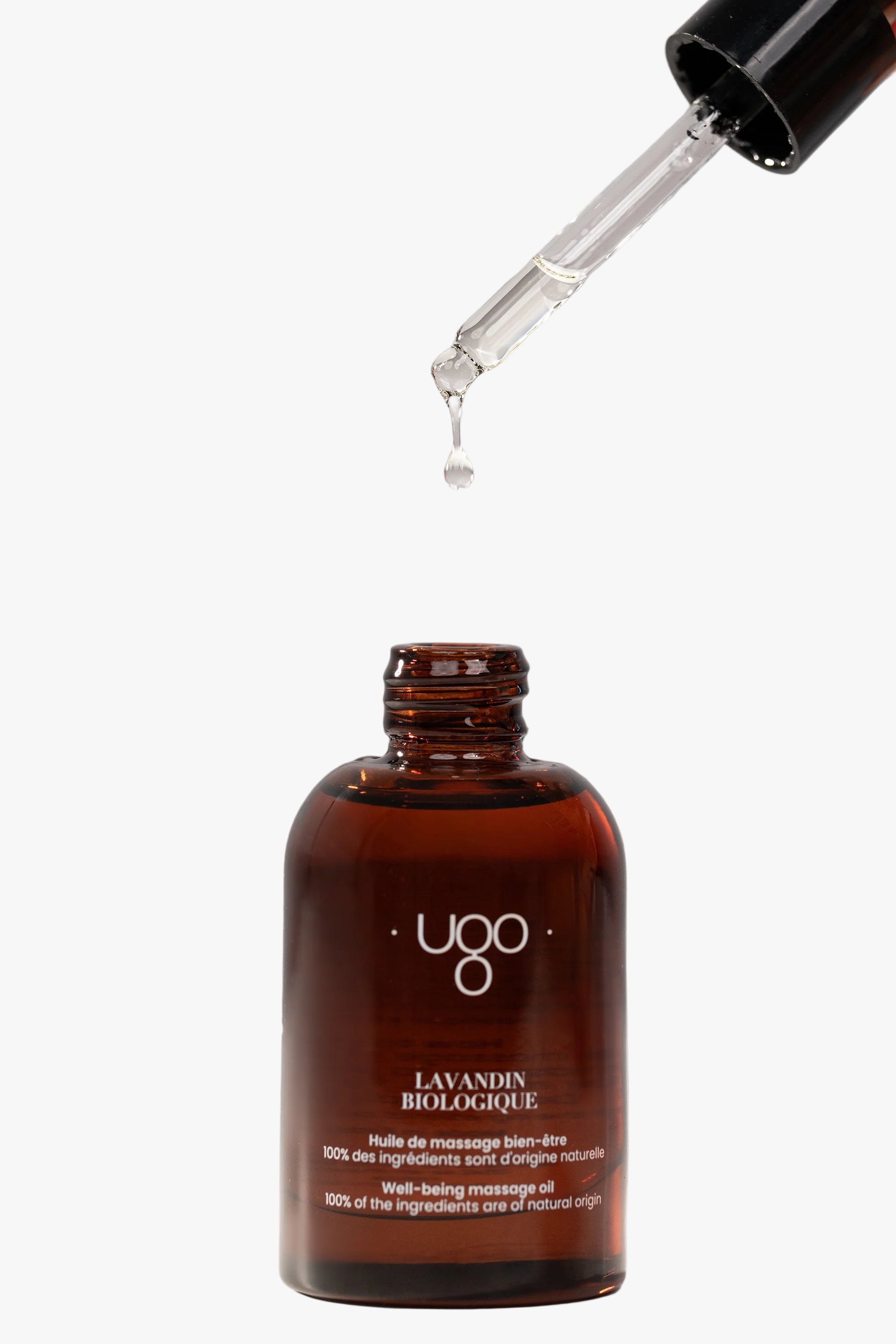 Pipette d’huile de massage Terre Ugo tenue à la main avec goutte en formation, vue rapprochée.